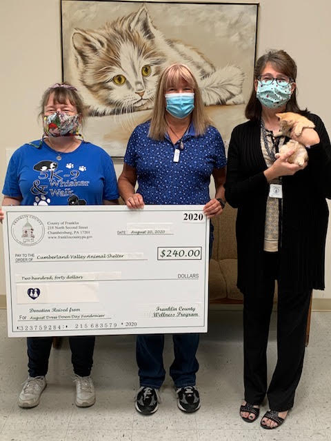 two women holding a check next to a woman holding a kitten