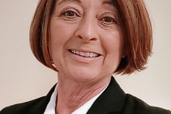 Person with short brown hair wearing a black blazer and white shirt smiles at the camera.