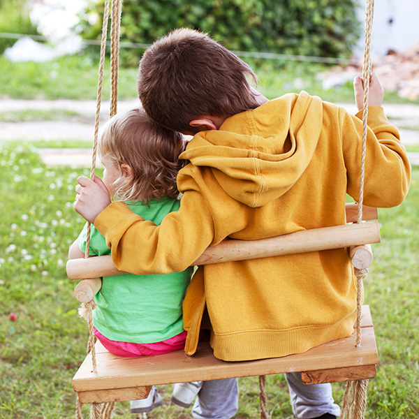 children sitting on a swing in the garden. older brother hugging little sister