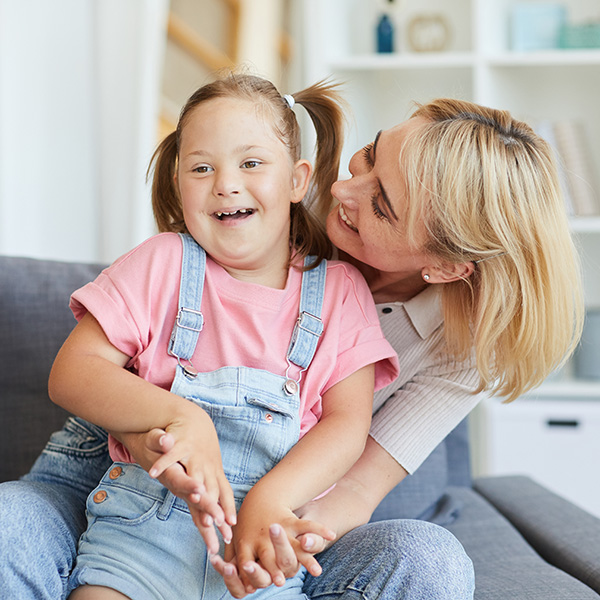 Young mother embracing her disabled child while they sitting on sofa in the room