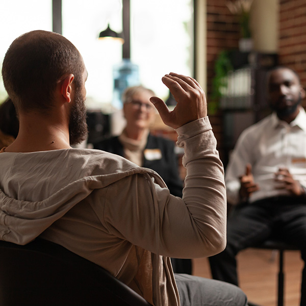 Man with addiction sharing mental health issues with group at aa meeting, talking to therapist.