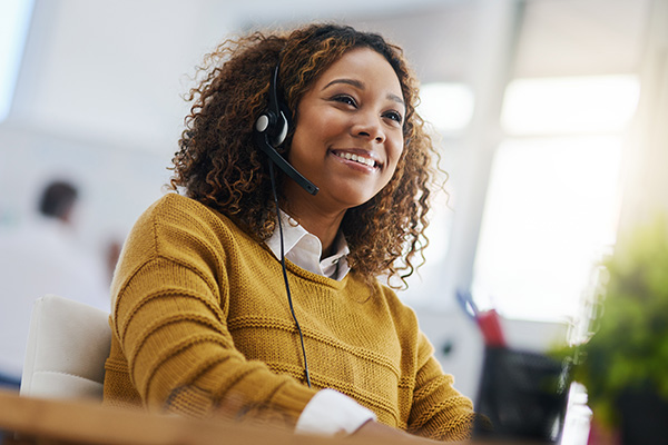 A smiling woman answers the phone to provide support.