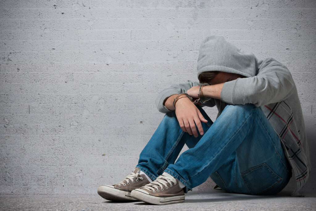 youth in handcuffs, sitting with knees up and face buried in arms.