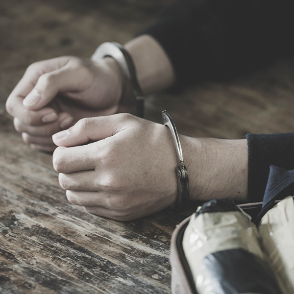 Close up of hands in handcuffs and a package on a table.