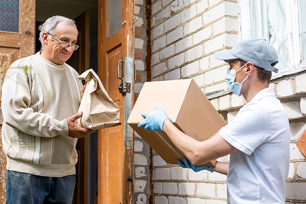 A volunteer bringing packages to a senior citizen at home.