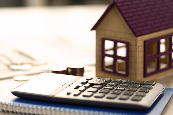 A model house next to a calculator and coins.