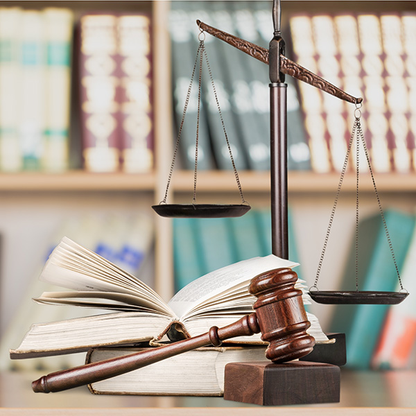 Scales of justice with a gavel and open book, with law books behind on a shelf.