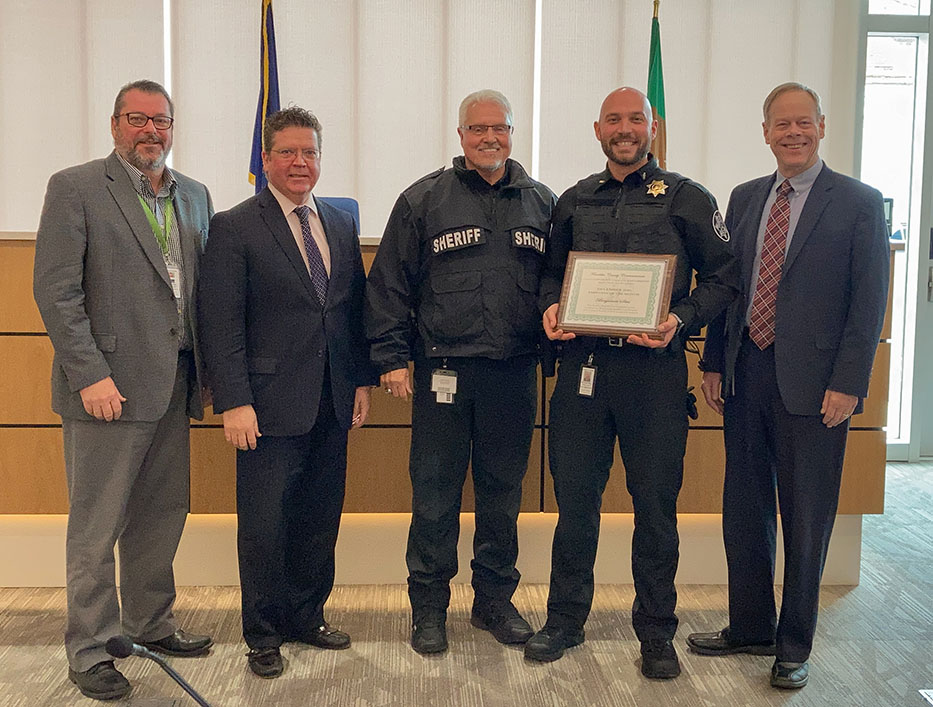 Five men standing in a row; two wearing sheriff uniforms, one holds a framed certificate.