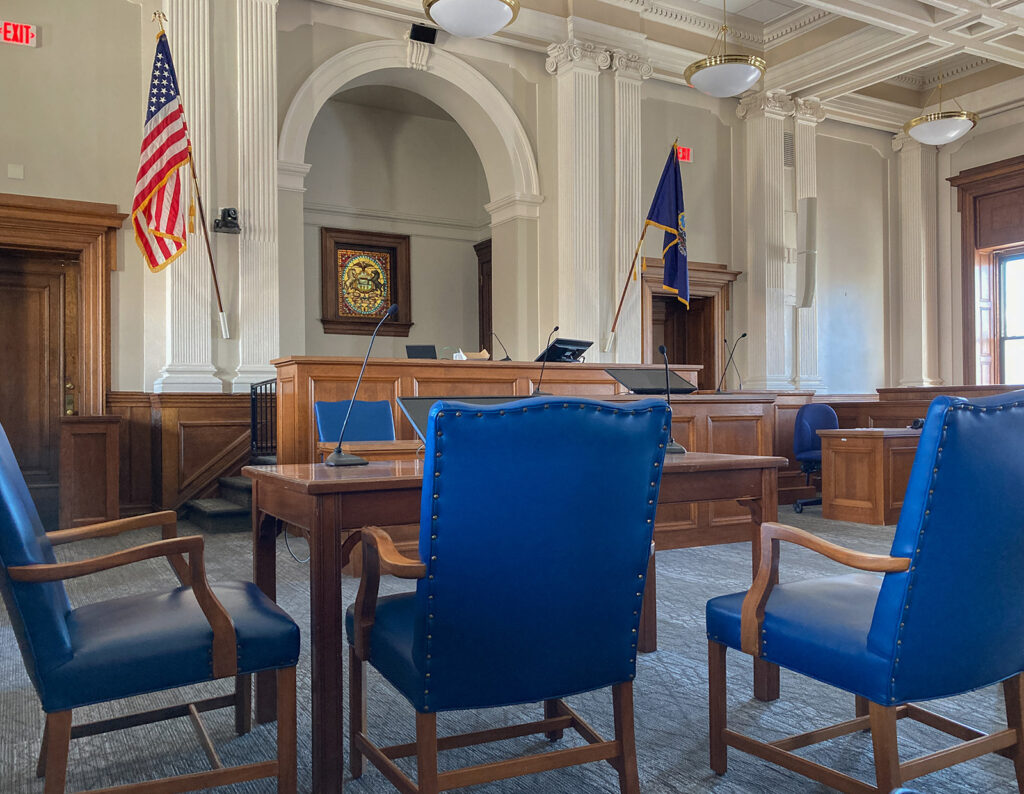 The interior of a courtroom with blue chairs.