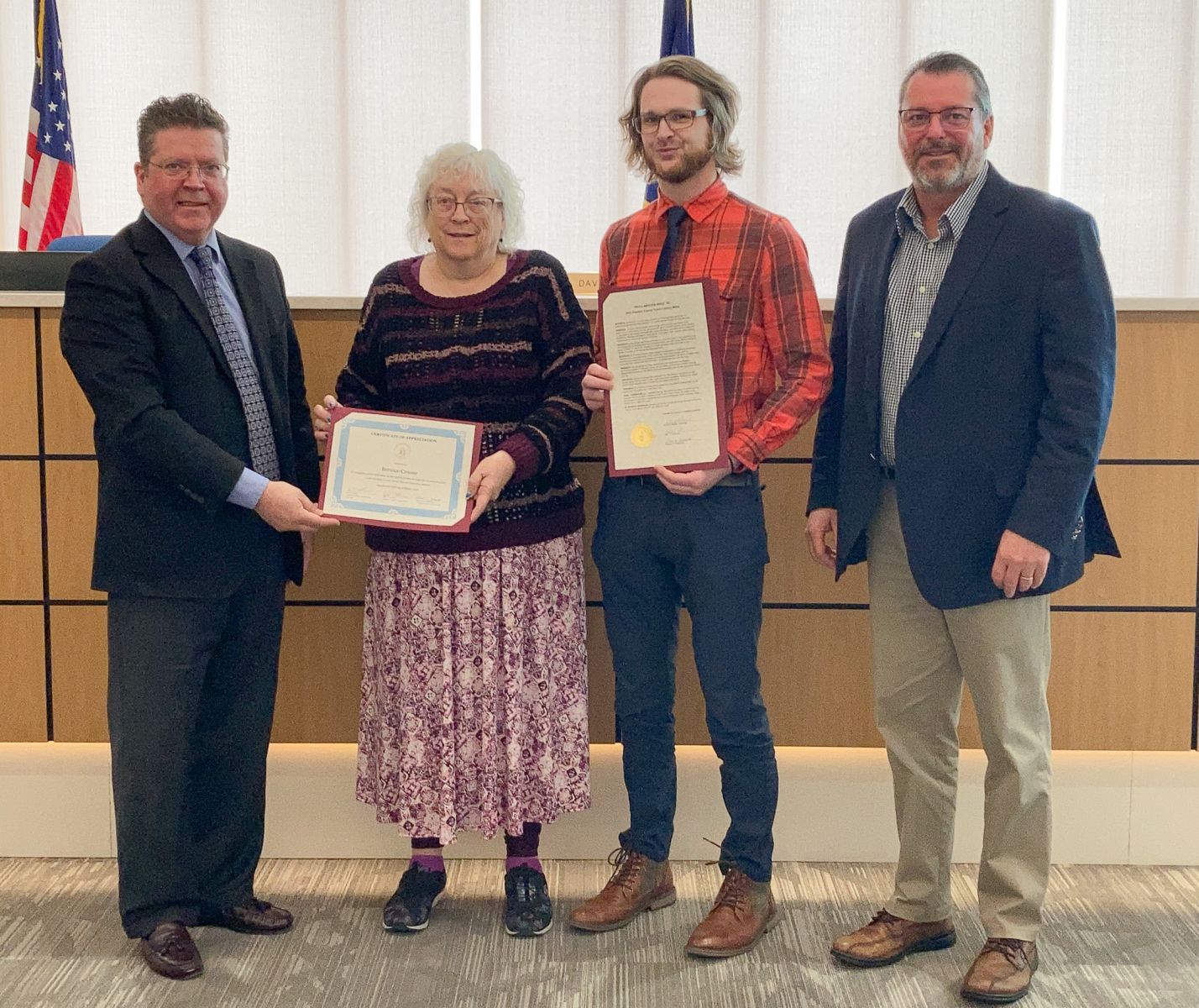 Four people standing in a room; two hold certificates.