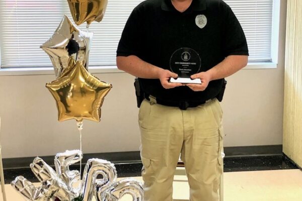 A person in uniform, wearing a mask, holds an award. 