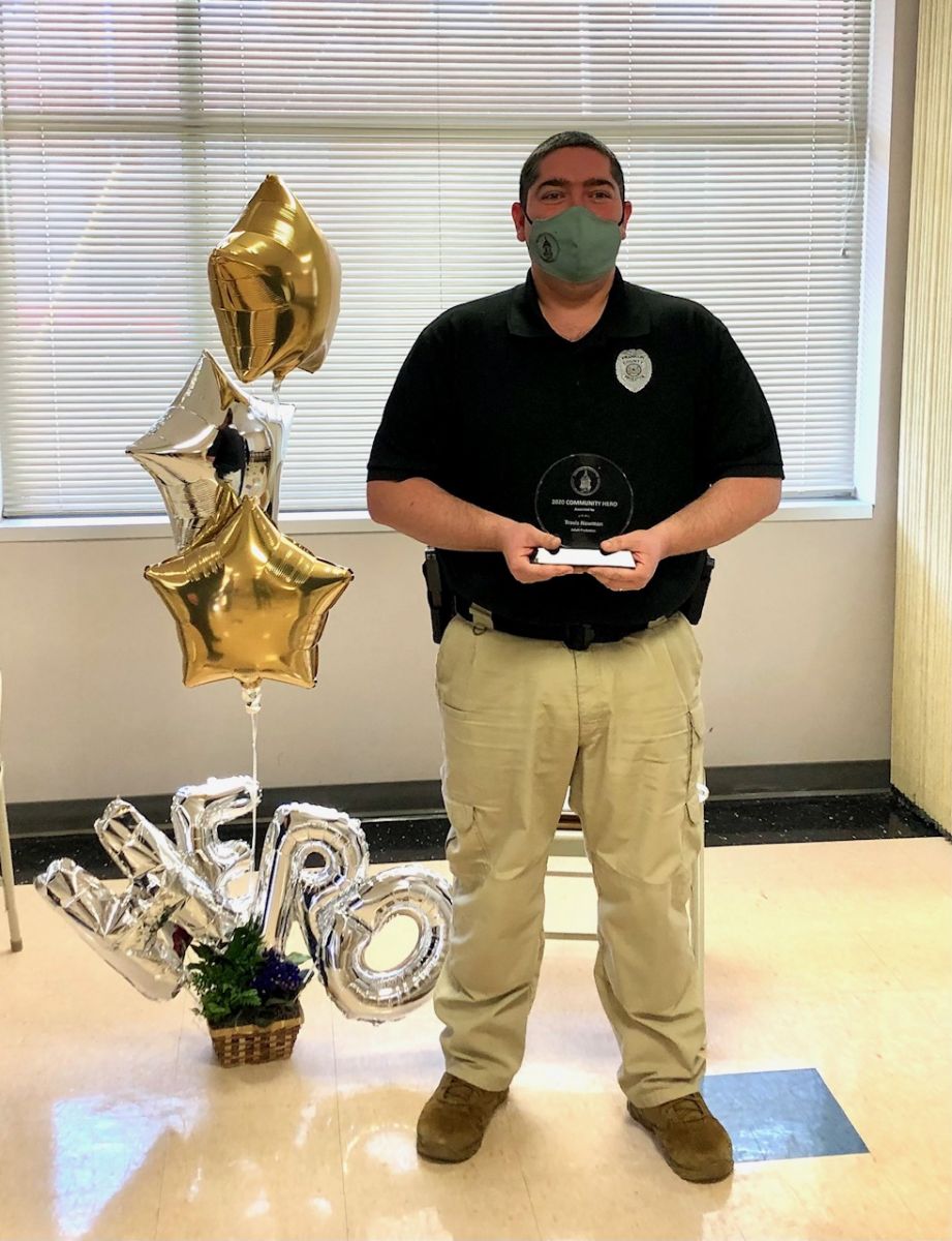 A person in uniform, wearing a mask, holds an award. 