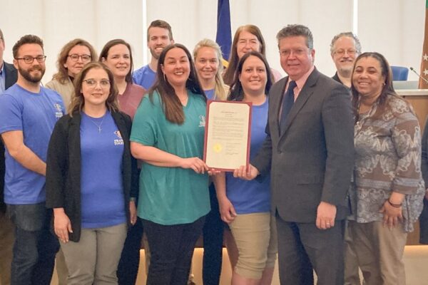 A group of people stand together in a room, with one person holding a certificate. They appear to be in a formal setting.