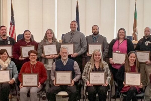 A group of people is standing and sitting in a room, holding certificates.