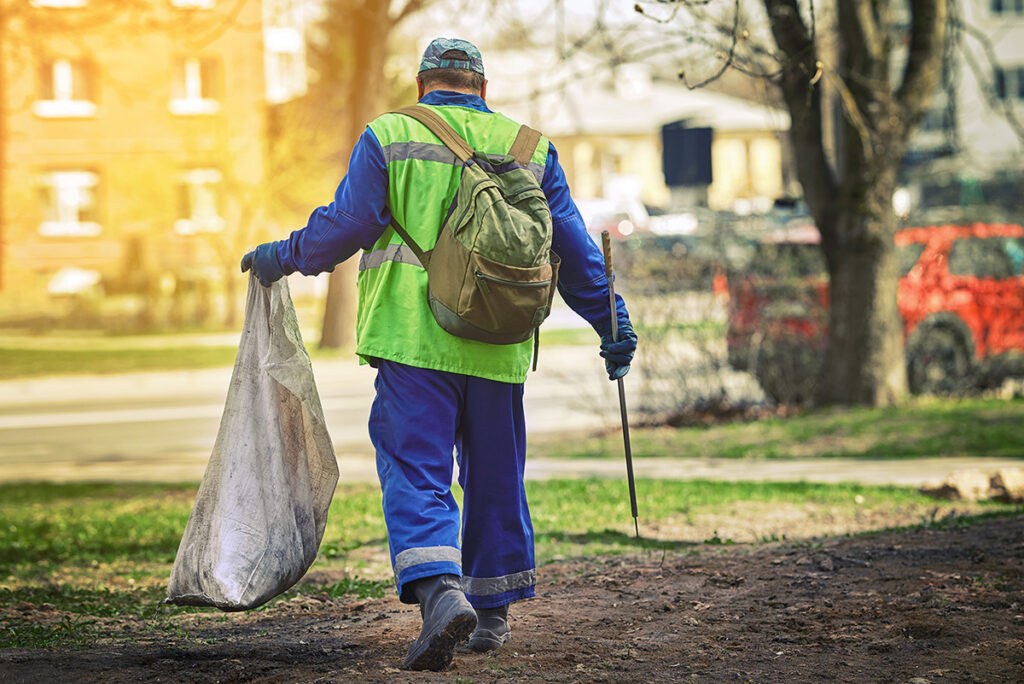 Utility worker with plastic bag and pick up tool for gathering paper, trash, plastic or metal cans. 