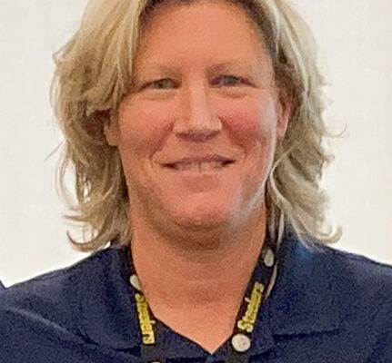 Person wearing a navy blue polo shirt with a badge and a lanyard, smiling at the camera.