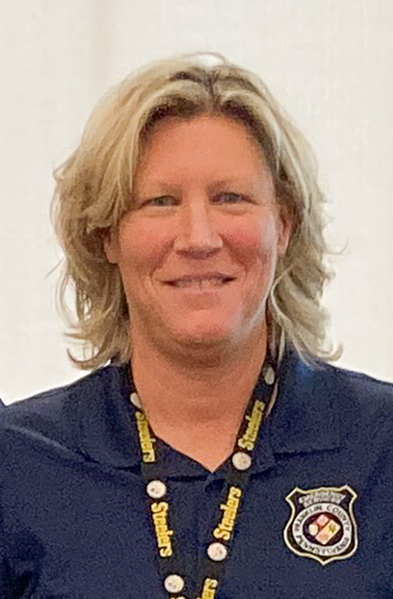 Person wearing a navy blue polo shirt with a badge and a lanyard, smiling at the camera.