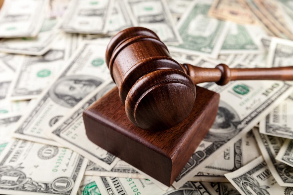 A wooden gavel rests on a block over a pile of U.S. dollar bills.