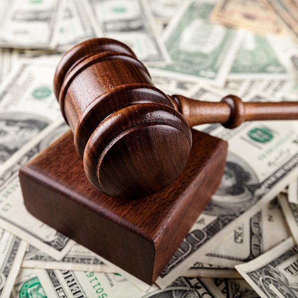 A wooden gavel rests on a block, surrounded by U.S. dollar bills.